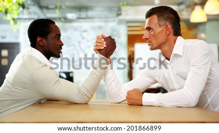 Portrait of two businessmen sitting opposite each other elbowing on the table with their arms grappled in fight