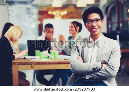 Portrait of cheerful businessman with arms folded sitting in front of colleagues
