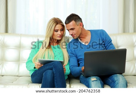 Young couple sitting on the sofa and using tablet computer with laptop at home