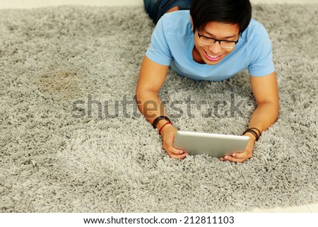 Happy asian man lying on the carpet with tablet computer