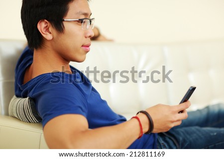 Asian man lying on the sofa and using smartphone at home