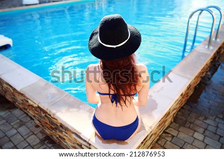 Back view portrait of a young woman sitting on the ledge of the pool