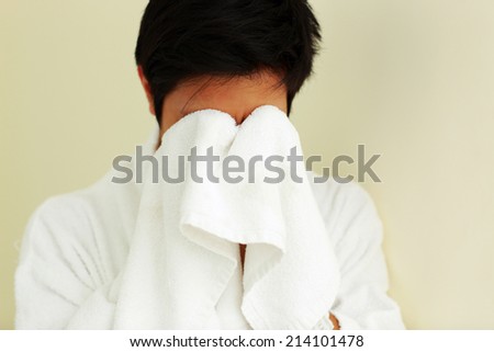 Young man in bathrobe wiping face with a towel