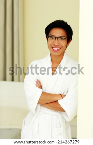 Happy asian man in bathrobe standing with arms folded at home