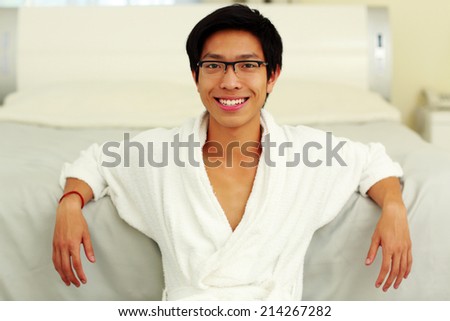 Happy man in bathrobe leaning on the bed in bedroom