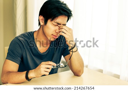 Tired asian man with eye pain holding glasses in hand