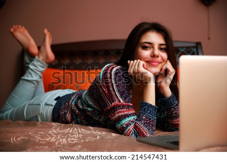 Cheerful woman lying on the bed with laptop