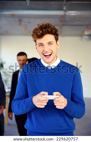 Laughing young businessman standing with smartphone in office