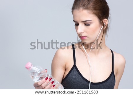 Portrait of a sporty woman in headphones looking on the bottle with water