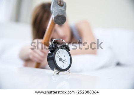 Woman not wanting to get up, taking a hammer to her alarm clock. Focus on clock