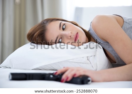 Portrait of a woman lying on the bed with gun