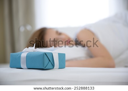 Woman sleeping on the bed with presents standing near her. Focus on gift