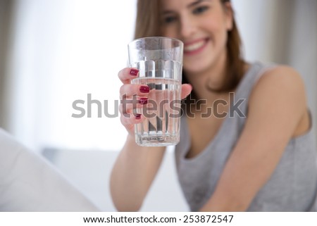 Portrait of a happy woman holding glass of water. Focus on glass