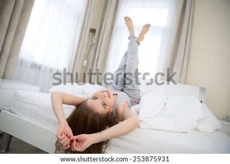 Happy young woman lying on the bed with raised legs up