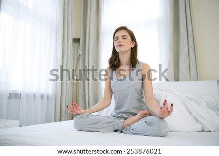 Young woman doing yoga exercises on the bed at home