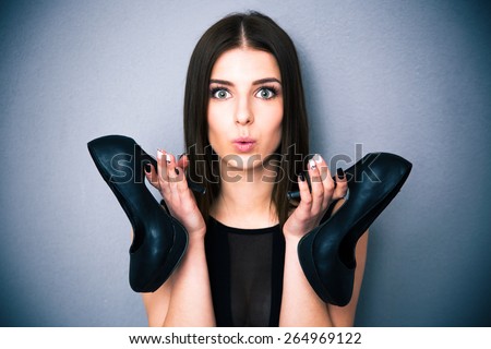 Portrait of a beautiful woman holding shoes. Wearing in sexy black dress. Looking at camera.