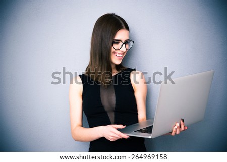 Happy woman standing with laptop over gray background. Wearing in fashion black dress. Looking at laptop