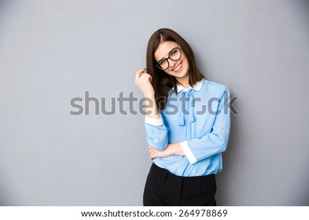 Smiling businesswoman in glasses standing over gray background. Wearing in blue shirt and glasses. Looking at camera