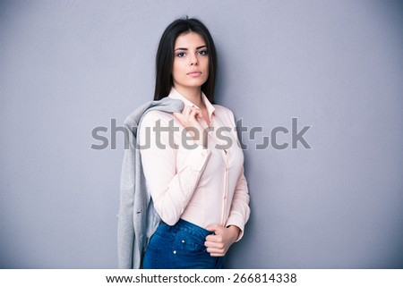 Young beautiful woman holding jacket on a shoulder over gray background. Looking at camera