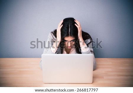 Tired businesswoman sitting at the table over gray background. Looking on laptop
