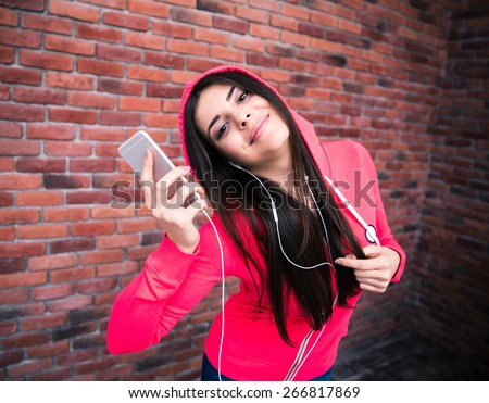Happy sportive cute woman listening music on smartphone over brick wall