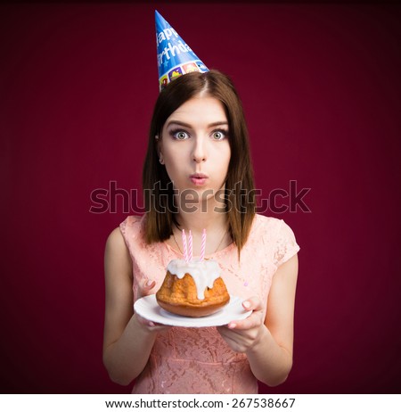 Young woman blowing candles on her cake over pink background. Looking at camera