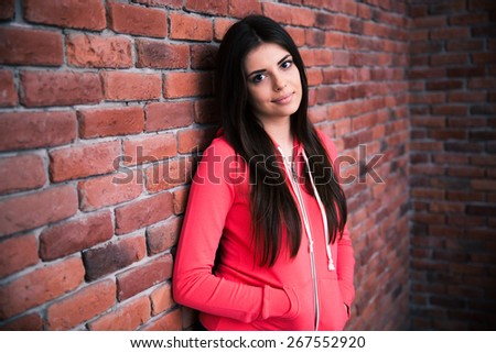 Portrait of attractive woman leaning on the brick wall and looking at camera