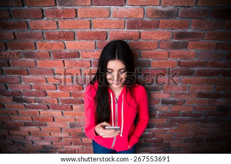 Happy woman using smartphone over brick wall. Wearing in sportive jacket