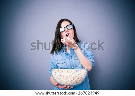 Cute woman in cinema glasses eating popcorn over gray background
