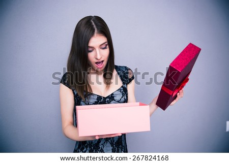Happy surprised woman opening gift box over gray background. Wearing in dress. Looking on present
