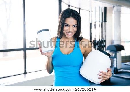 Smiling woman holding plastic container with sports nutrition at gym