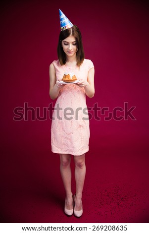 Full length portrait of a happy woman holding cake with candles over pink background. Wearing in dress