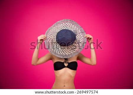 Woman in bikini covering her face with hat over pink background