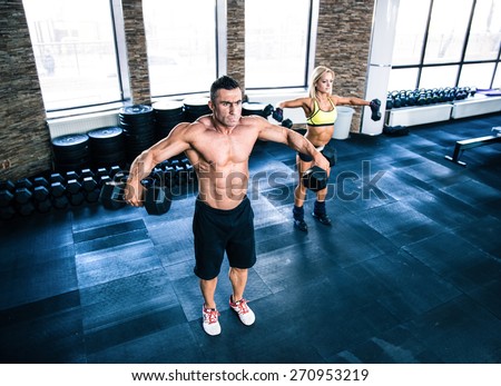 Muscular man and fit woman workout with dumbbells at gym