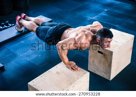 Muscular man doing push ups on fit box and bench at gym