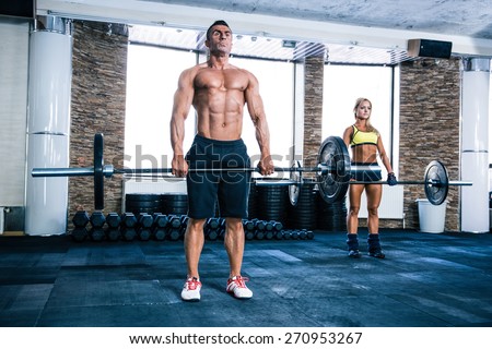 Muscular man and woman workout with barbell at gym