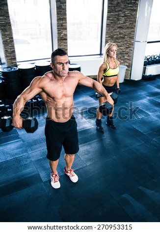 Muscular man and fit woman lifting dumbbells at gym