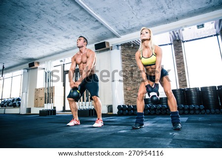 Muscular man and fit woman lifting kettle ball at gym