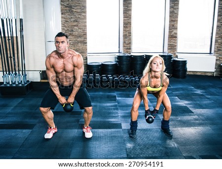 Muscular man and fit woman doing exercises with kettle ball at gym