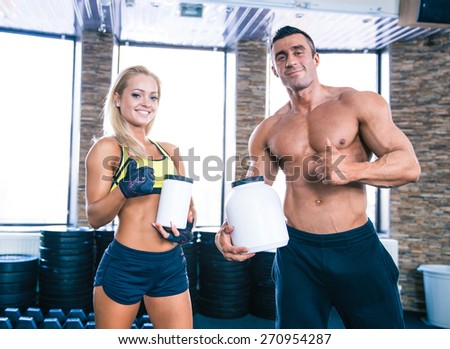 Muscular man and sporty woman holding container with sports nutrition and showing thumb up