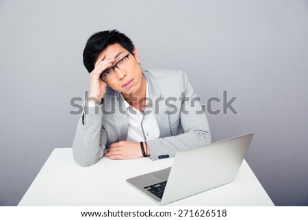 Asian businessman sitting at the table with laptop and looking at camera over gray background