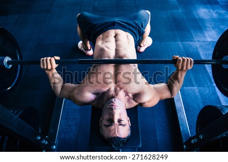 Muscular man workout with barbell on bench at gym