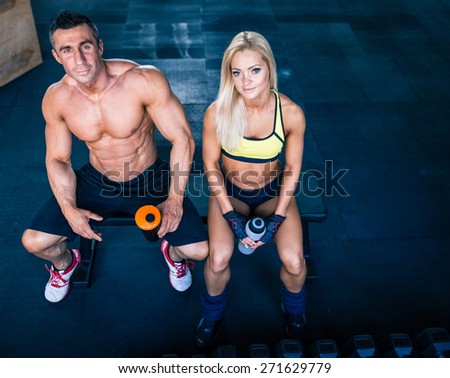 Muscular man and fit woman sitting on the bench at gym and looking at camera