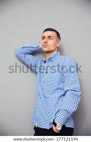 Portrait of a pensive young man in shirt standing over gray background. Looking away