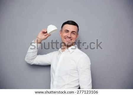 Cheerful businessman holding white cup over gray background and looking at camera