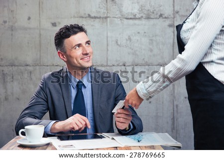 Happy confident man giving bank card to female waiter in restaurant