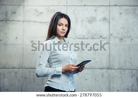 Portrait of a beautiful businesswoman with tablet computer standing over concrete wall and looking at camera