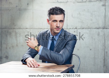 Handsome businessman sitting at the table and looking at camera over concrete wall