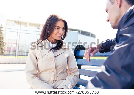 Happy woman talking with man outdoors. Sitting on the bench. Looking at each other