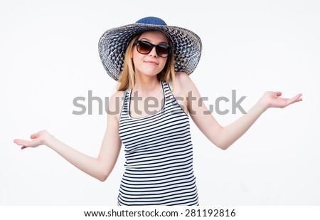 Happy woman in hat and sunglasses shrugging her shoulders over gray background